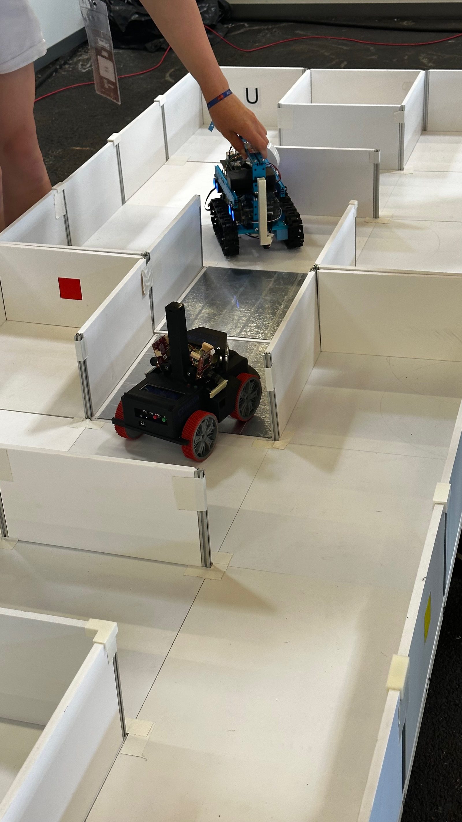 Un robot de RoboCupJunior Rescue avanzando por un laberinto de paredes blancas con una rampa entre habitaciones.