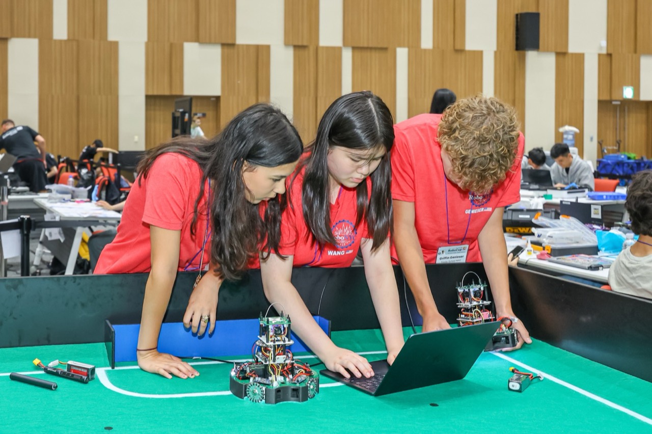 Students crouched over their soccer robots at the field side, laptop open